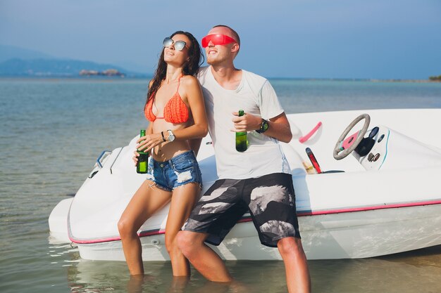 Glückliche Hipster-Frau und Mann, die Bier im tropischen Sommerurlaub in Thailand trinken, das auf Boot im Meer reist, Party am Strand, Leute, die Spaß zusammen haben, positive Emotionen