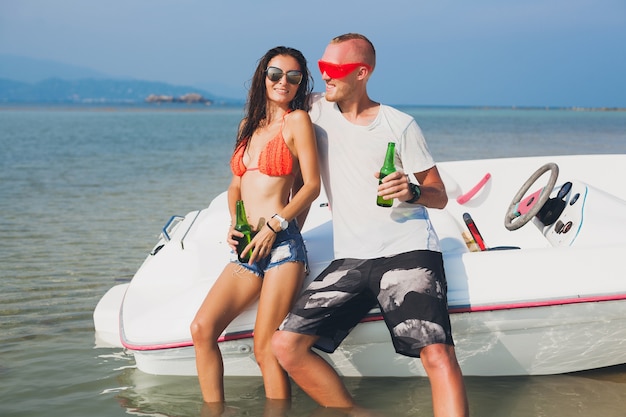 Glückliche Hipster-Frau und Mann, die Bier im tropischen Sommerurlaub in Thailand trinken, das auf Boot im Meer reist, Party am Strand, Leute, die Spaß zusammen haben, positive Emotionen