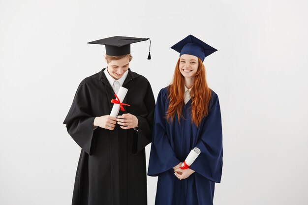 Glückliche Hochschulabsolventen in den lächelnden Mänteln, die Diplome halten.