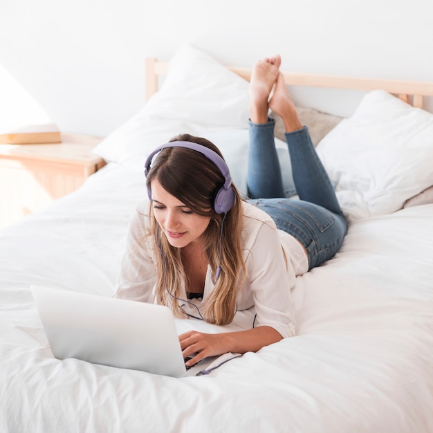 Glückliche hörende Musik der jungen Frau auf dem Bett