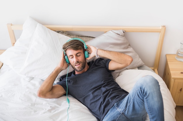 Glückliche hörende Musik des jungen Mannes auf dem Bett