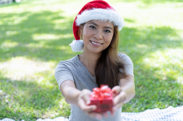 Glückliche hübsche asiatische Dame, die Sankt-Hut trägt und Geschenkbox gibt