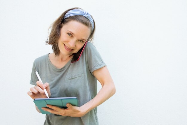 Glückliche hübsche Frau, die auf Tablettbildschirm schreibt