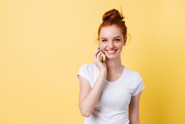 Glückliche Ingwerfrau im T-Shirt, das durch das Smartphone spricht