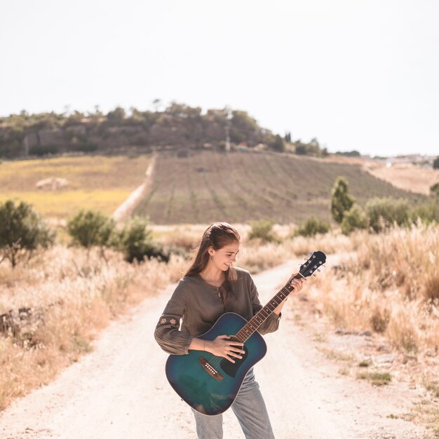 Glückliche Jugendliche, die auf der Sandbahn spielt Gitarre steht