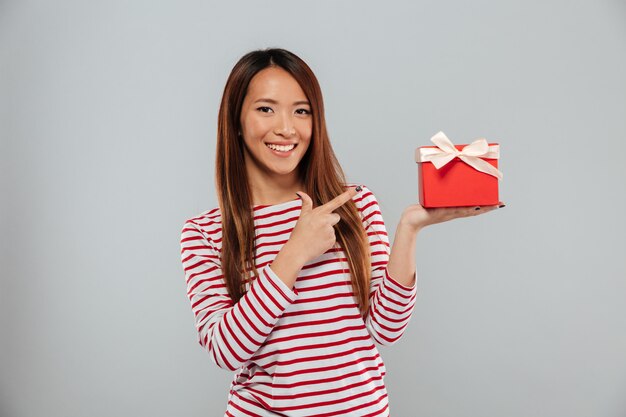 Glückliche junge asiatische Dame, die isoliert hält Geschenk hält und zeigt.