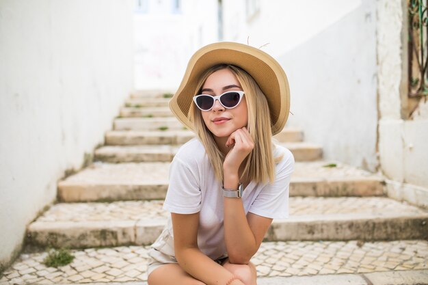 Glückliche junge blonde Frau in Hut und Sonnenbrille lachend