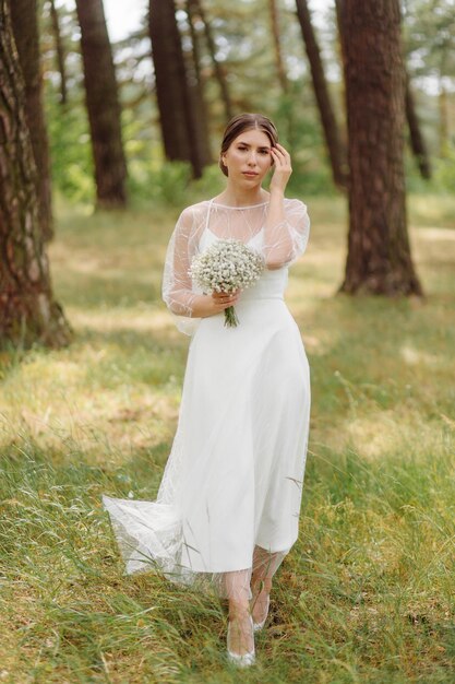 Glückliche junge Braut in einem weißen Hochzeitskleid des Kiefernwaldes