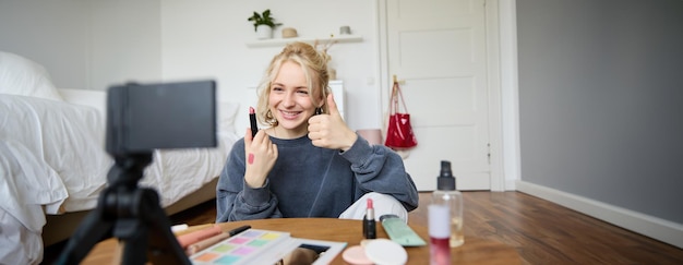 Kostenloses Foto glückliche junge content-schöpferin zeigt lippenstift, lifestyle-beauty-vlog auf digitaler kamera