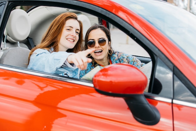 Glückliche junge Dame, die auf nette Frau zeigt und im Auto sitzt