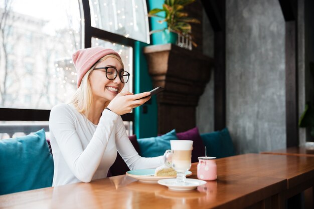 Glückliche junge Dame machen Foto von Kuchen und Kaffee