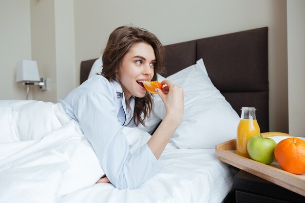 Glückliche junge Dame unter Decke, die Orange isst.