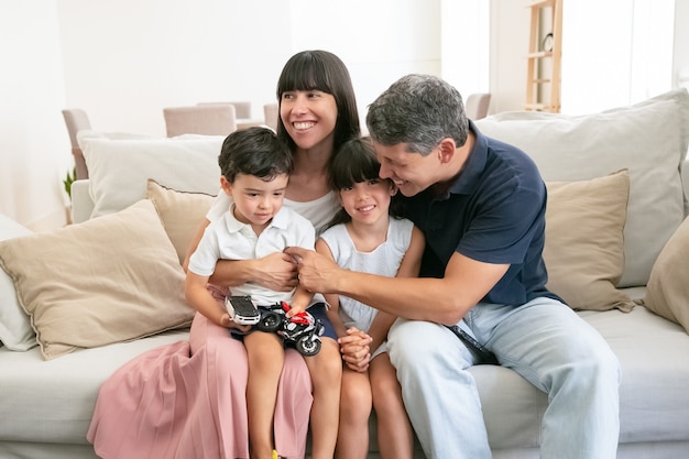 Glückliche junge familie, die zusammen auf sofa sitzt und lächelt.