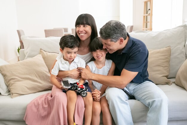 Glückliche junge Familie, die zusammen auf Sofa sitzt und lächelt.