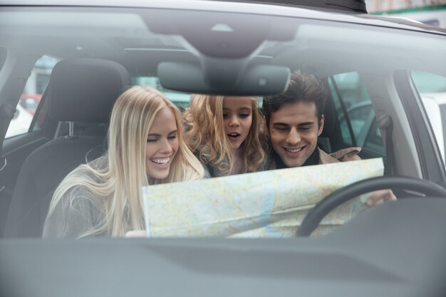 Glückliche junge Familie im Auto, das Karte hält.