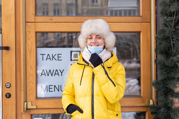 Glückliche junge Frau an der Tür des Restaurants an einem kalten Wintertag, Schriftzug, Essen zum Mitnehmen.