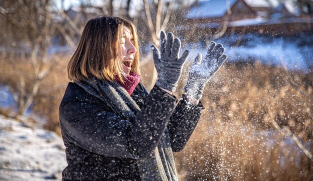 Glückliche junge Frau auf einem Spaziergang im Winter mit Schnee in den Händen