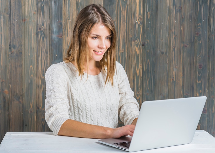 Kostenlose Foto glückliche junge frau, die an laptop gegen hölzerne wand arbeitet