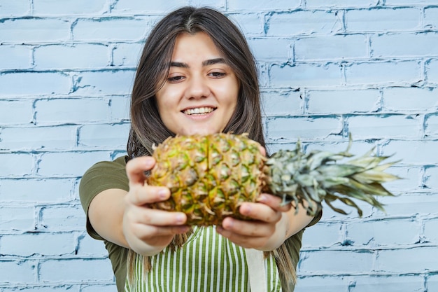 Glückliche junge Frau, die Ananas auf blauer Oberfläche hält