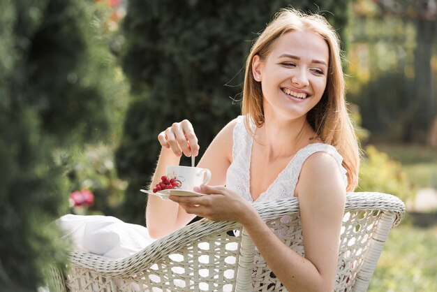 Glückliche junge Frau, die auf rührendem Kaffee des weißen Stuhls mit Löffel sitzt