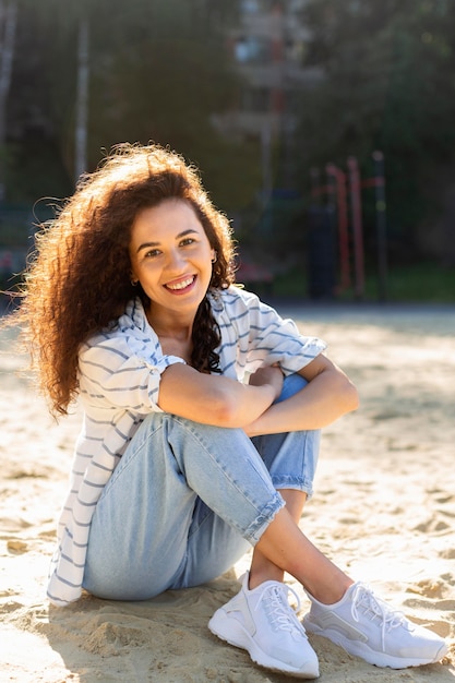 Kostenloses Foto glückliche junge frau, die beim sitzen auf sand aufwirft