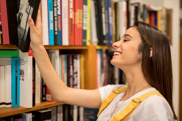 Glückliche junge Frau, die Buch vom Bücherregal nimmt