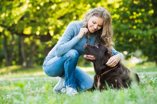 Glückliche junge Frau, die ihren Hund im Park betrachtet