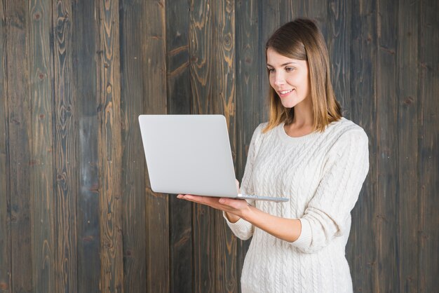 Glückliche junge Frau, die Laptop gegen hölzernen Hintergrund hält
