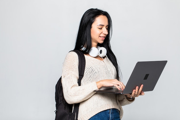 Glückliche junge Frau, die Laptop und über graue Wand hält