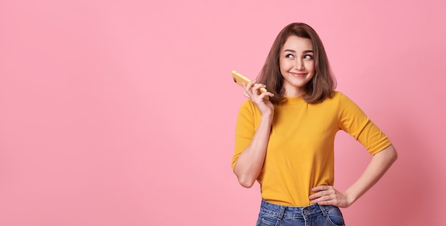 Glückliche junge Frau, die mit dem Handy lokalisiert über rosa Hintergrund feiert.