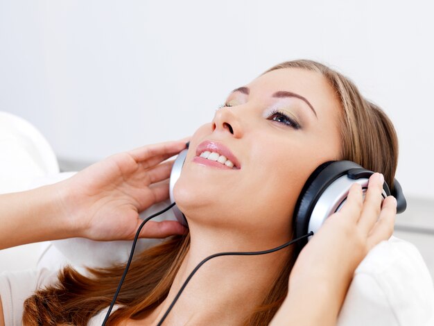 Glückliche junge Frau, die Musik im Kopfhörer hört - drinnen