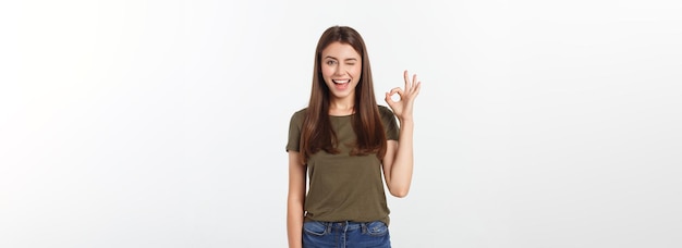 Glückliche junge Frau, die ok Zeichen mit den Fingern ein Zwinkern lokalisiert auf einem grauen Hintergrund zeigt