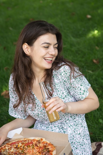 Glückliche junge Frau, die Pizza bei einem Picknick isst