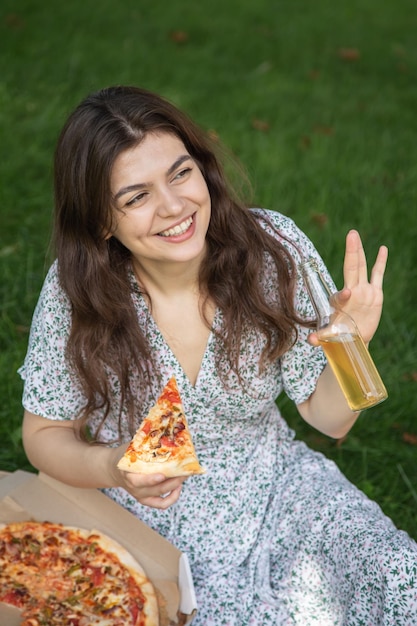 Glückliche junge frau, die pizza bei einem picknick isst