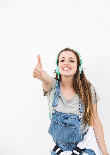 Glückliche junge frau, die thumbup zeichen gegen weißen hintergrund zeigt