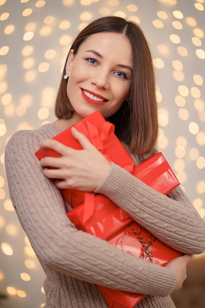 Glückliche junge Frau, die viele Geschenkkästen mit Lichtern hält