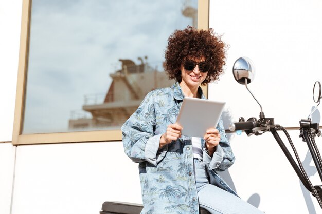 Glückliche junge Frau in der Sonnenbrille unter Verwendung des Tablet-Computers