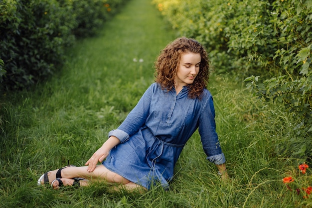 Glückliche junge Frau mit braunem lockigem Haar, ein Kleid tragend, im Freien in einem Garten posierend