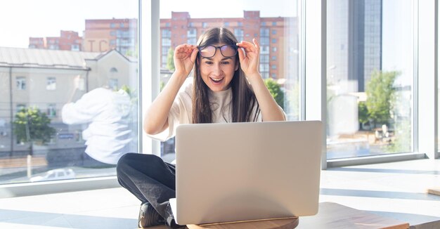 Glückliche junge Frau mit Brille vor einem Laptop-Bildschirm