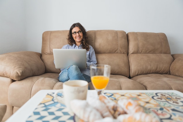 Glückliche junge Frau mit Laptop auf dem Sofa sitzt