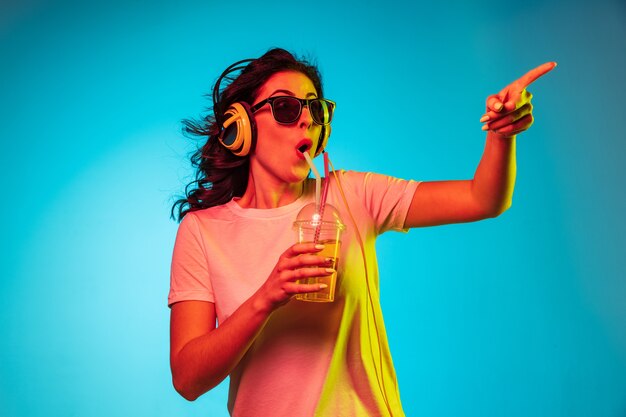 Glückliche junge Frau tanzt und lächelt in Kopfhörern über trendigem blauem Neon