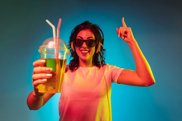 Glückliche junge Frau tanzt und lächelt in Kopfhörern über trendigem blauem Neonstudio