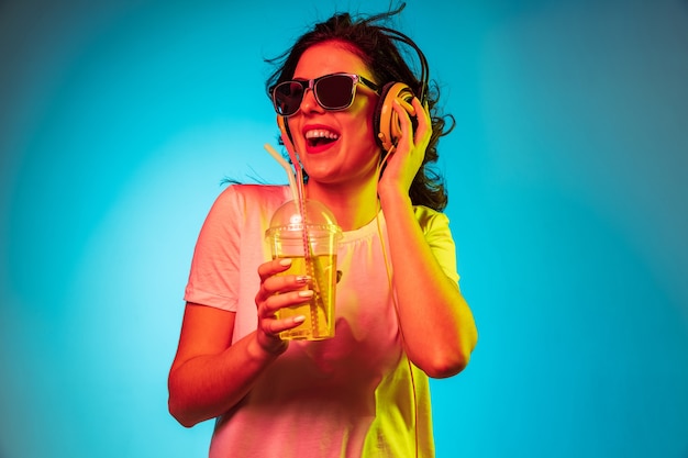 Glückliche junge Frau tanzt und lächelt in Kopfhörern über trendigem blauem Neonstudio