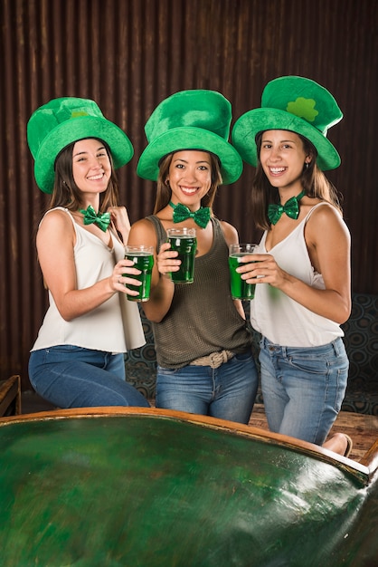 Glückliche junge Frauen, die Gläser des Getränks nahe Tabelle halten