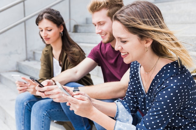 Glückliche junge Freunde, die auf Treppenhaus unter Verwendung des Mobiltelefons sitzen