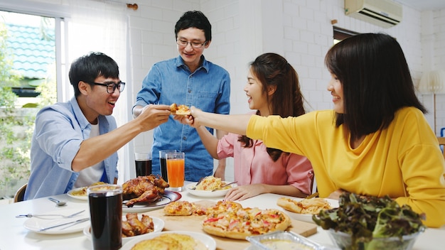 Glückliche junge Freunde Gruppe, die zu Hause zu Mittag isst. Asia Familienfeier, die Pizza Essen isst und lachend das Essen genießt, während sie am Esstisch zusammen im Haus sitzt. Festurlaub und Zusammengehörigkeit.