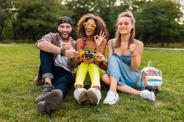 Glückliche junge Freunde sitzen Park mit Smartphones