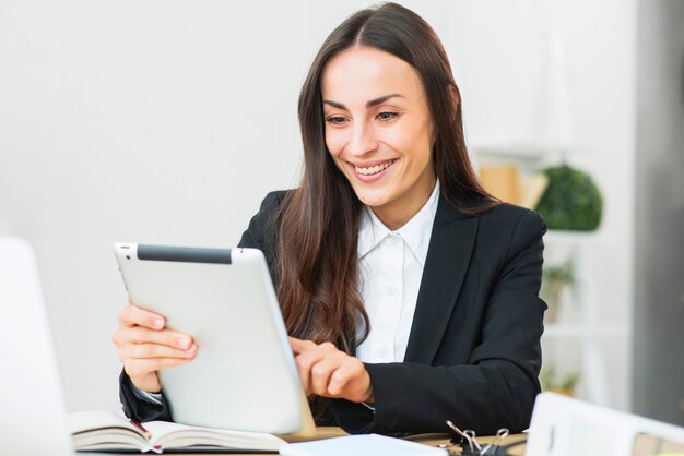 Glückliche junge Geschäftsfrau, die digitale Tablette im Büro verwendet