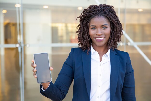 Glückliche junge Geschäftsfrau, die Smartphone zeigt