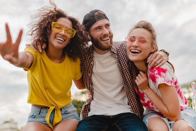 Glückliche junge Gesellschaft lächelnder Freunde, die im Park aufgeregt sind, Mann und Frau, die zusammen Spaß haben